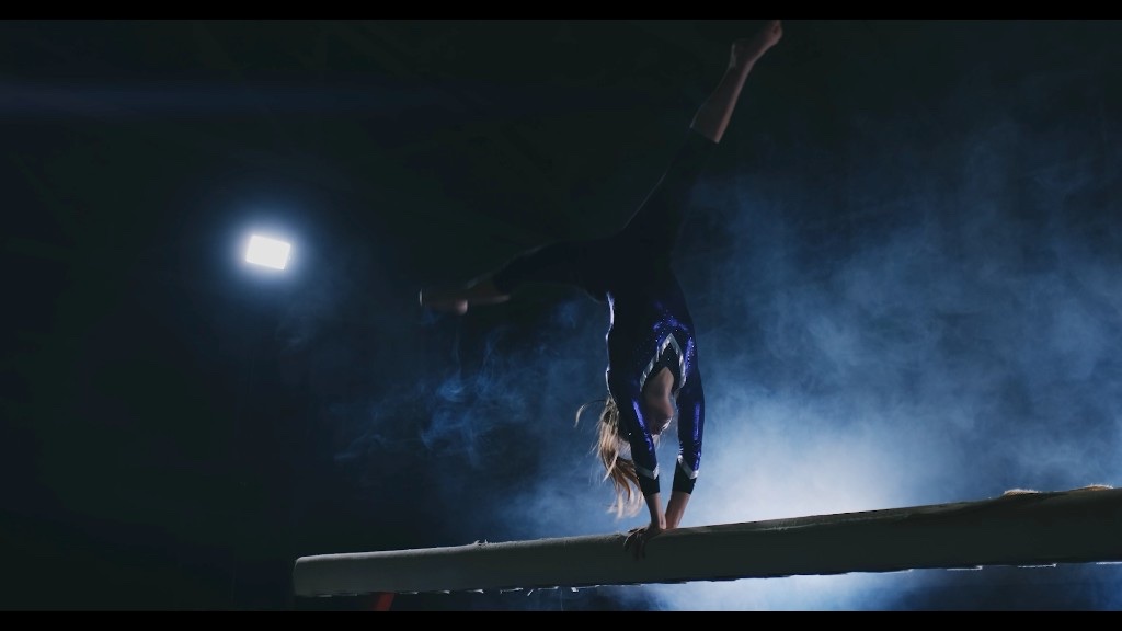 A gymnast stands in fog and backlight before competition, arms open